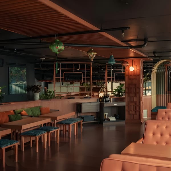 A dimly lit restaurant interior with orange and green seating, wooden tables, and decorative lanterns.