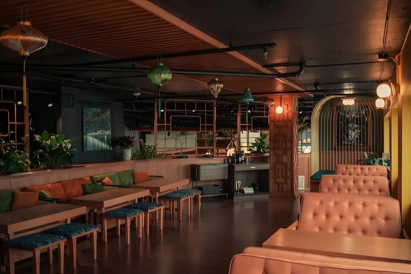 A dimly lit restaurant interior with orange and green seating, wooden tables, and decorative lanterns.