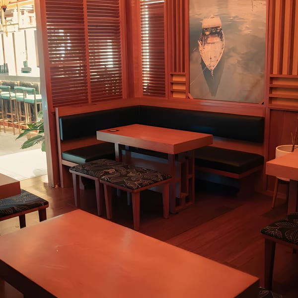 Cozy restaurant interior with wooden tables, black booth seating, and a boat painting on the wall.