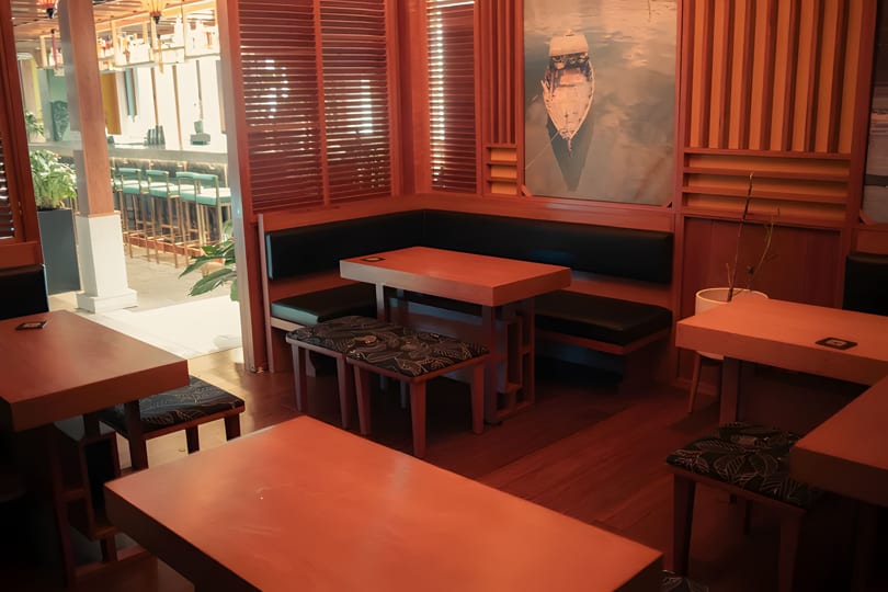 Cozy restaurant interior with wooden tables, black booth seating, and a boat painting on the wall.