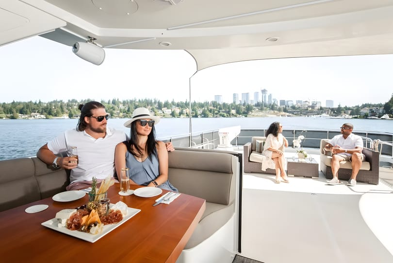 Two couples relaxing on a yacht, enjoying drinks and a charcuterie board with a city skyline view.