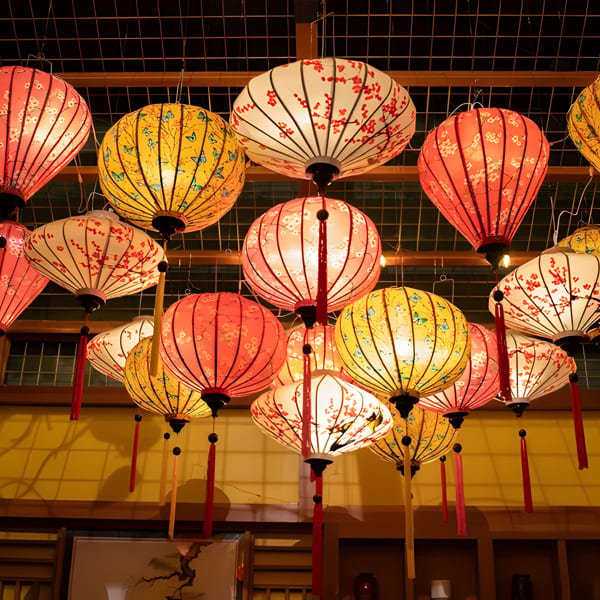 Numerous colorful, illuminated paper lanterns with floral and butterfly patterns hang from a ceiling.