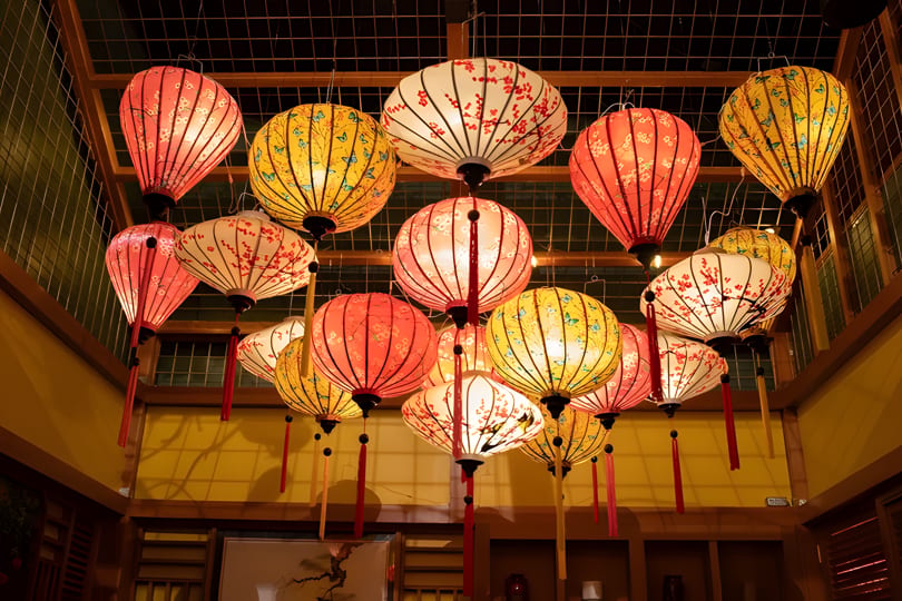 Numerous colorful, illuminated paper lanterns with floral and butterfly patterns hang from a ceiling.