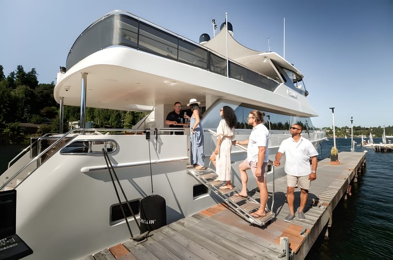 People boarding a large white yacht from a wooden dock on a sunny day.