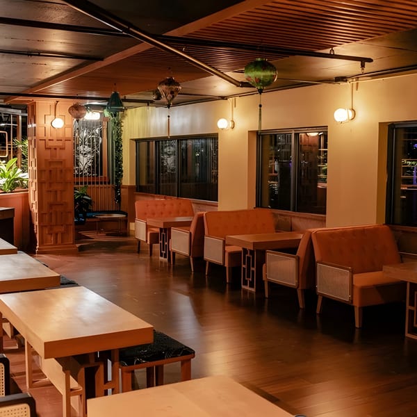 A dimly lit restaurant interior with wooden tables, orange banquettes, and decorative lanterns.