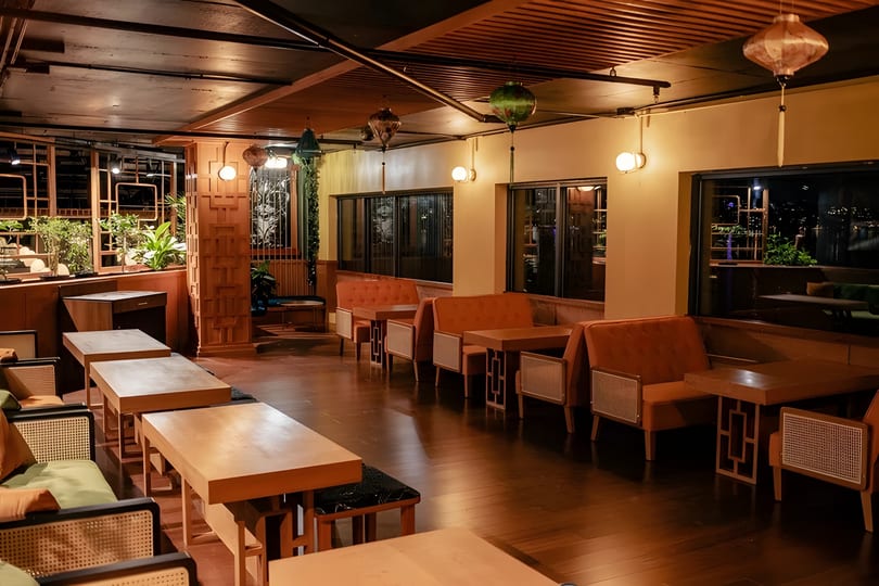A dimly lit restaurant interior with wooden tables, orange banquettes, and decorative lanterns.