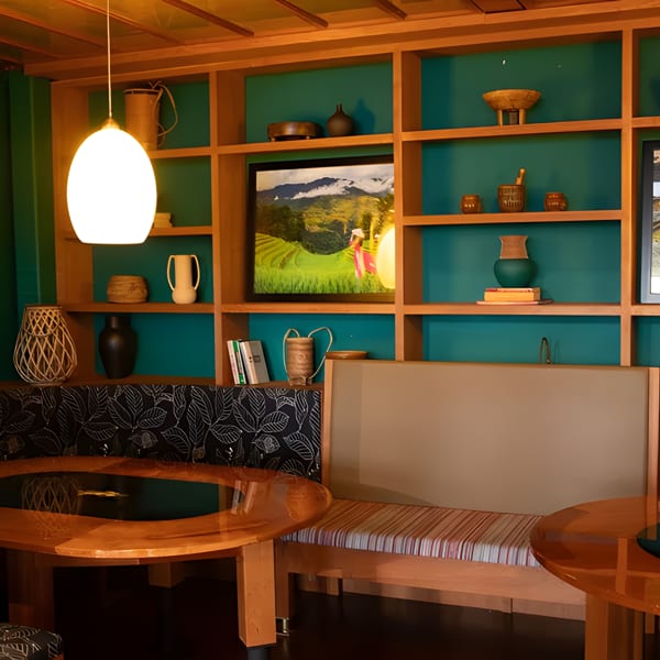 A restaurant interior with green walls, wooden shelves displaying decor, and booth seating with round tables.