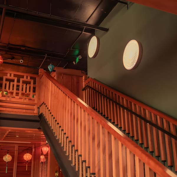 Warmly lit wooden staircase with decorative lanterns and circular wall art in a restaurant.