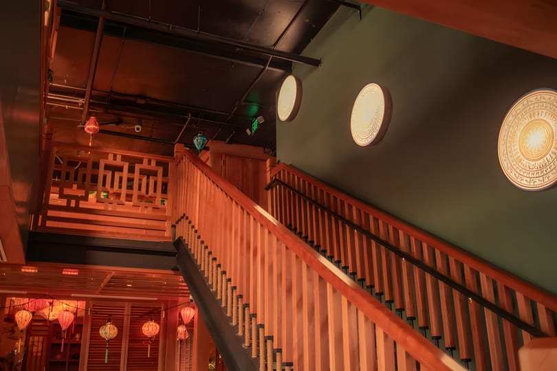 Warmly lit wooden staircase with decorative lanterns and circular wall art in a restaurant.