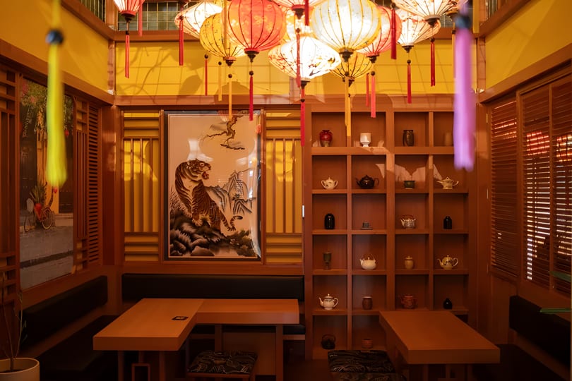 A cozy restaurant interior with wooden tables, benches, a tiger painting, and hanging lanterns.
