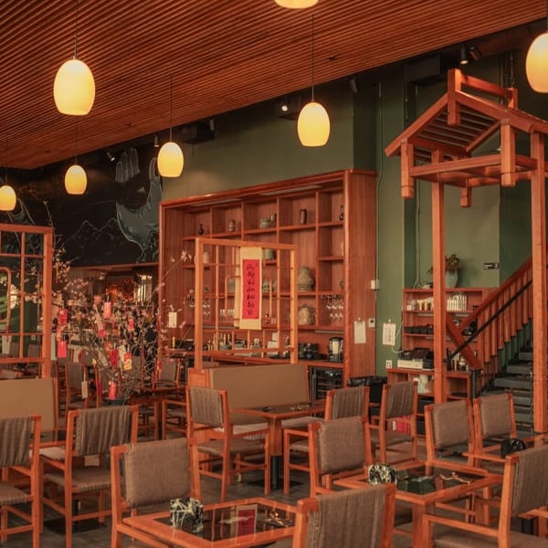 A restaurant interior with wooden furniture, green walls, hanging lights, and a decorative wooden archway.