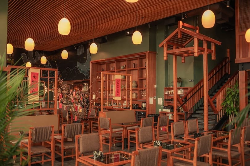 A restaurant interior with wooden furniture, green walls, hanging lights, and a decorative wooden archway.