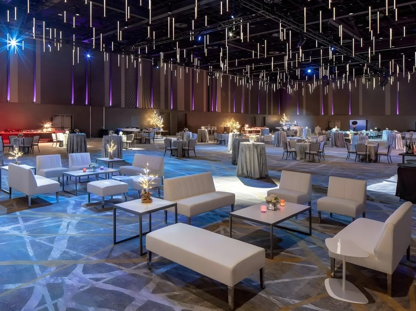 A large, modern event space with lounge seating, cocktail tables, and dramatic overhead lighting.