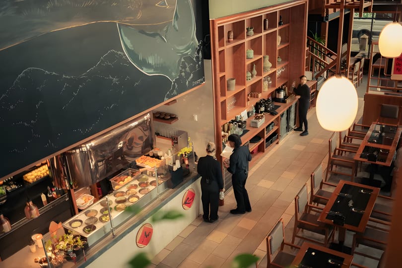Overhead view of a modern restaurant interior with a food counter, dining tables, and staff.
