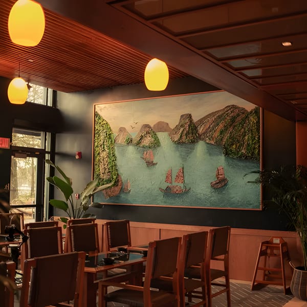 Restaurant interior with a large painting of boats on water, wooden tables, and warm lighting.