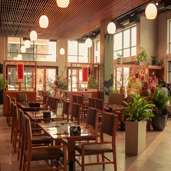 Spacious restaurant dining room with wooden tables and chairs, large windows, and decorative plants.