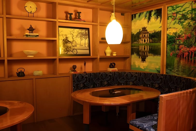 A cozy restaurant booth with a wooden table, shelves, and large scenic wall art.