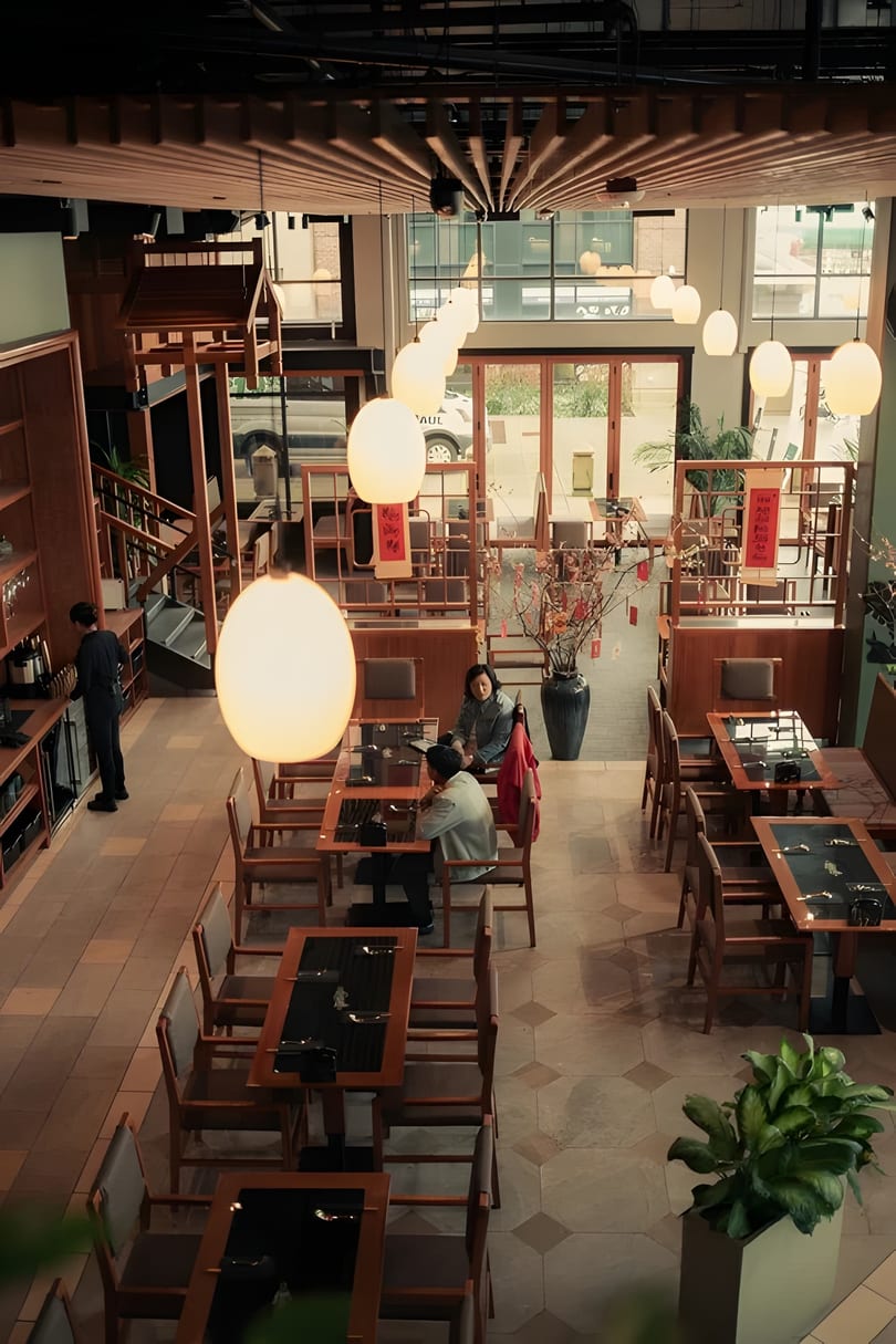 Overhead view of a restaurant dining room with wooden tables, chairs, and glowing pendant lights.