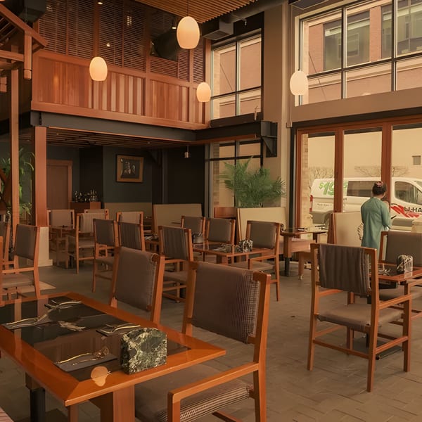 Spacious restaurant interior with wooden tables and chairs, a grand staircase, and large windows.