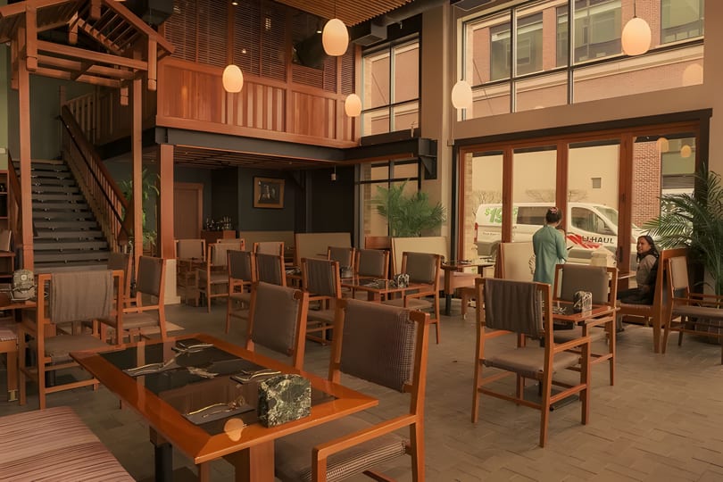 Spacious restaurant interior with wooden tables and chairs, a grand staircase, and large windows.